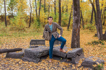 Fototapeta premium Tall handsome man with a bag standing near the rocks in the autumn forest