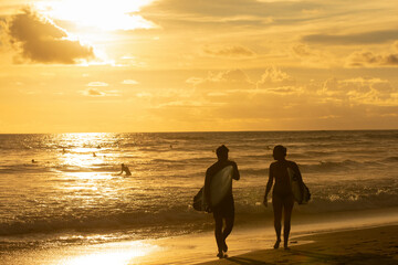 Couple of surfers leaving the water after surfing on a beautiful golden sunset at the beach. Body board and surf lifestyle concept.