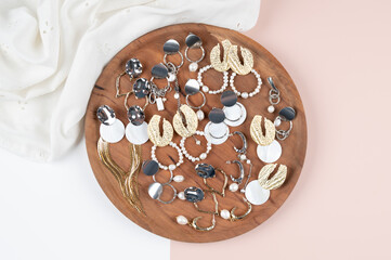 Top view of a lot of stylish earrings on a wooden tray. Women's jewelry. Pink and white surface