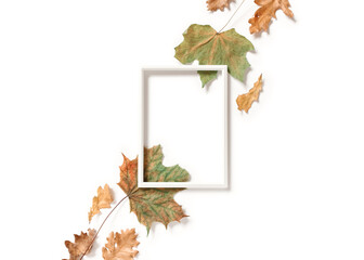 Minimalistic autumn composition. An empty photo frame and diagonal maple and oak leaves are on a white background. Flat lay. Top view. Copy space.
