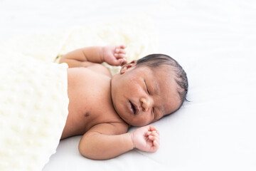 Obraz na płótnie Canvas Top view of Newborn baby sleeping with blanket on white bed. Infant lying on white bed. African American newborn baby. Afro infant
