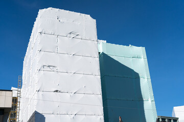 Mufti-story building in shrink-wrap to protect workers inside and public on outside from risks...