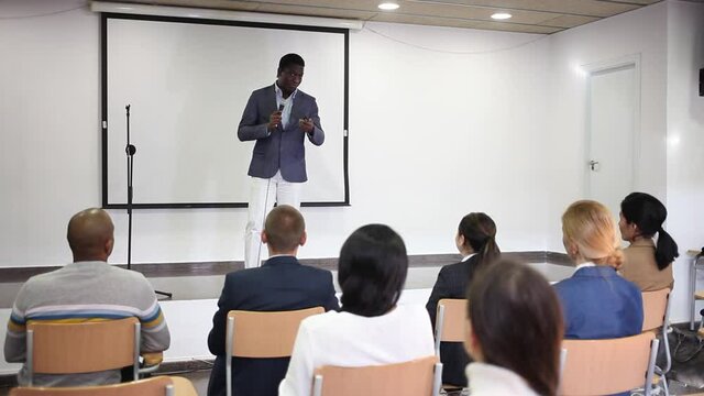 Successful aframerican business coach speaking from stage to audience at corporate training