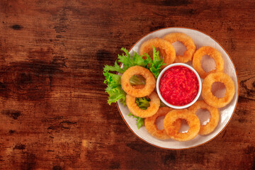 Squid rings. Calamari rings with green salad leaves and ketchup, overhead shot on a dark rustic wooden background with copy space