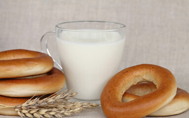 bagels, wheat ears and a glass of milk on a linen background