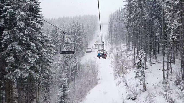 Wonderful winter scene with snow falling while climbing to the top of the mountain on a cable car gondola. Bukovel ski resort in Ukrainian Carpathians. Ski lift passing through the snowy fir forest