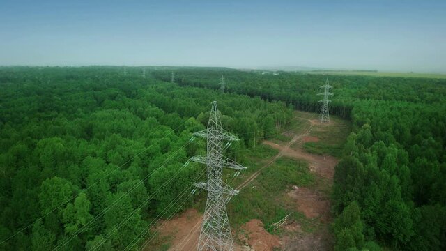 Electric high voltage alternative energy power transmission line tower extending into the forest. Green ecology forest. Drone aerial view.