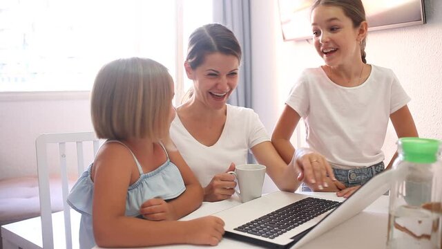 Cheerful woman with two kids sitting at table in living room and using computer