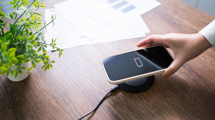 Charging mobile phone battery with wireless charging device in the table. Smartphone charging on a charging pad. Mobile phone near wireless charger Modern lifestyle technology concept.