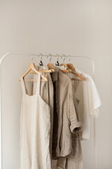 Minimal aesthetic fashion clothes concept. Neutral beige washed linen female blouses, dresses and t-shirts on hanger on white background. Fashion blog, website, social media