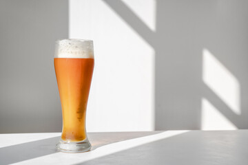 Glass of beer on table against white wall with graphic shadows. Minimalistic still life with...