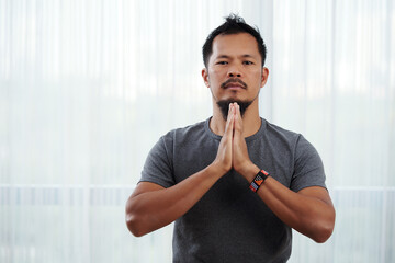Serious religious young man making namaste gesture and looking at camera
