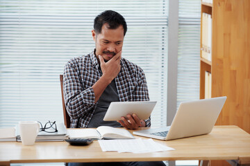 Pensive entrepreneur rubbing his chin when reading e-mail from client with confusing requirement...