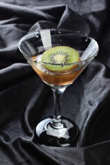 Fresh kiwi fruit slices are placed on a glass cup on a black background