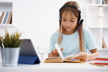 Little caucasian girl in headphones have video call distant class with teacher at home