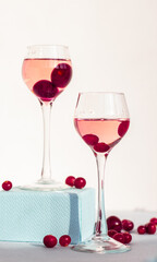 a pair of glasses of pink gin or vodka infused with cranberry among frozen berries closeup, a long-stemmed glass with cherry liqueur or any red alcoholic cocktail standing on blue box base