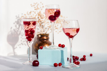 Fototapeta na wymiar set of glasses of pink gin or vodka infused with cranberry among frozen berries, a long-stemmed glass with cherry liqueur or any red alcoholic cocktail standing on blue box base