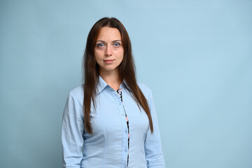 Portrait of a Caucasian young brunette woman in a blue shirt on a blue background stands smiling