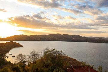 Beautiful sunset on the sea with hills and sun coming down under clouds sky