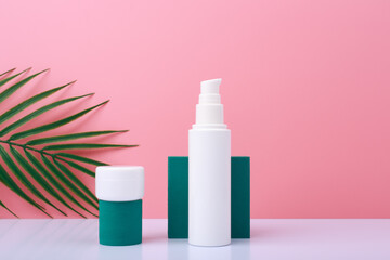 Creative trendy set with two white cosmetic jars with skin care products on green geometric shapes for product presentation on white table against pink background with palm leaf. 