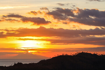 Obraz premium Sunset covered by mountain silhouettes with evening sky and dramatic clouds