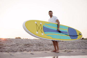 Young man carrying sup board after water surf session