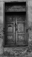 Black and white photo of a closed old wooden door with cracked paint in a house in old Riga
