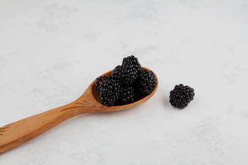 Blackberry or bramble in wooden spoon on light grey background. Close-up, selective focus, copy space