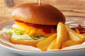 Fresh burger and potato wedges on gray wooden background
