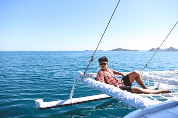 Asian man wearing sunglasses relaxing on catamaran net enjoying summer time