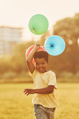 With balloons in hands. African american kid have fun in the field at summer daytime