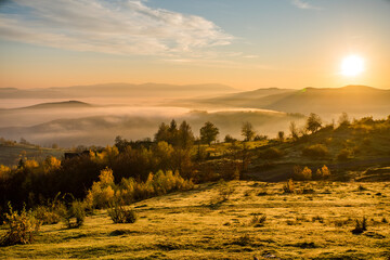 sunset in the mountains on a beautiful autumn day. fields and trees in the fog on a background of mountains in the sun. beautiful natural background.