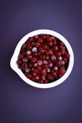 Frozen cranberry in white bowl on violet background. Selective focus. Flat lay of frozen cranberries.