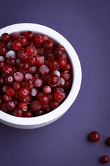 Frozen cranberry in white bowl on violet background. Selective focus. Close up of frozen cranberries.