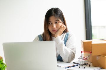 Young smiling beautiful owner asian woman freelance sme business online shopping working on laptop computer with parcel box on desk at home - SME business online and delivery concept