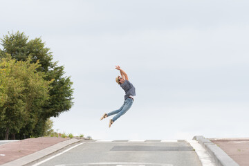 Young happy man jumping while crossing the road in the horizon. Happiness concept with copy space. Minimal composition