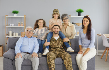 Portrait of a happy military man at home with his big family. Reunion with family. Soldier, his wife, children and older parents sit together on the sofa in the living room and look at the camera.