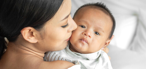 Portrait of enjoy happy love family asian mother playing with adorable little asian baby.Mom touching with cute son moments good time in a white bedroom.Love of family concept