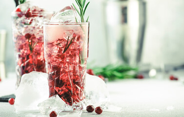 Cranberry cocktail with vodka, ice, juice, rosemary and red berries in highball glass. Refreshing long drink. Gray table background with negative space