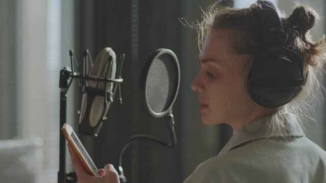 A young girl in monitor headphones in front of a microphone records a podcast