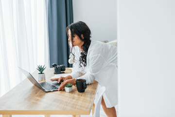 Wireless technology. Uses laptop. Woman in casual clothes is indoors at home