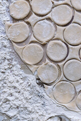 On a floured table there is a dough with unprofessional small circles prepared for dumplings