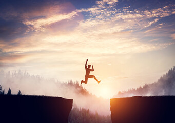Man jumping between cliffs at sunset.