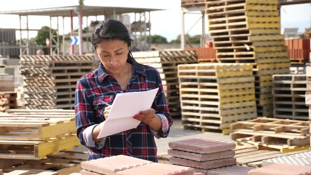 Concentrated hispanic woman worker controlling quantity of tiles at hardware store warehouse