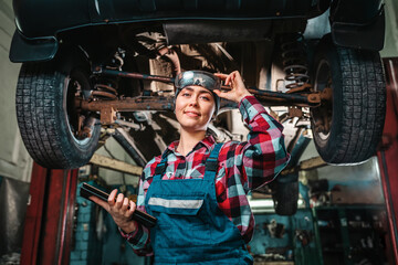 A young pretty smiling female mechanic, in a uniform, holding glasses, with a tablet in her hands,...