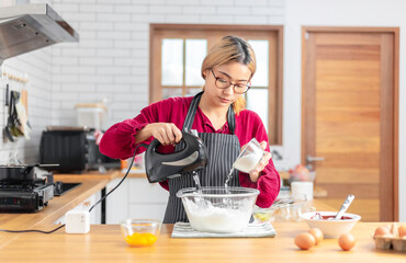 Asian girl using the blender, blend dough and other ingredients for cooking the chocolate cake with happy feeling in the kitchen room.