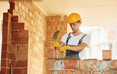 Bricks installation. Young man working in uniform at construction at daytime