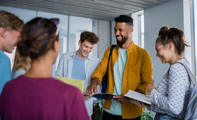 Group of university students standing in corridor indoors, talking and laughing.
