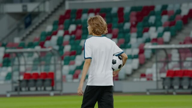 Portarit of Caucasian pre teen kid boy entering the field of huge soccer stadium, holding a ball, dreaming of becoming professional player, soccer star