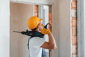 Empty walls. Young man working in uniform at construction at daytime